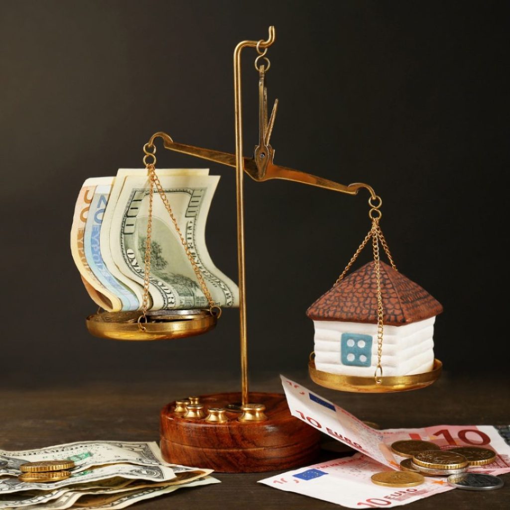 Balance scale weighing money against a house model.