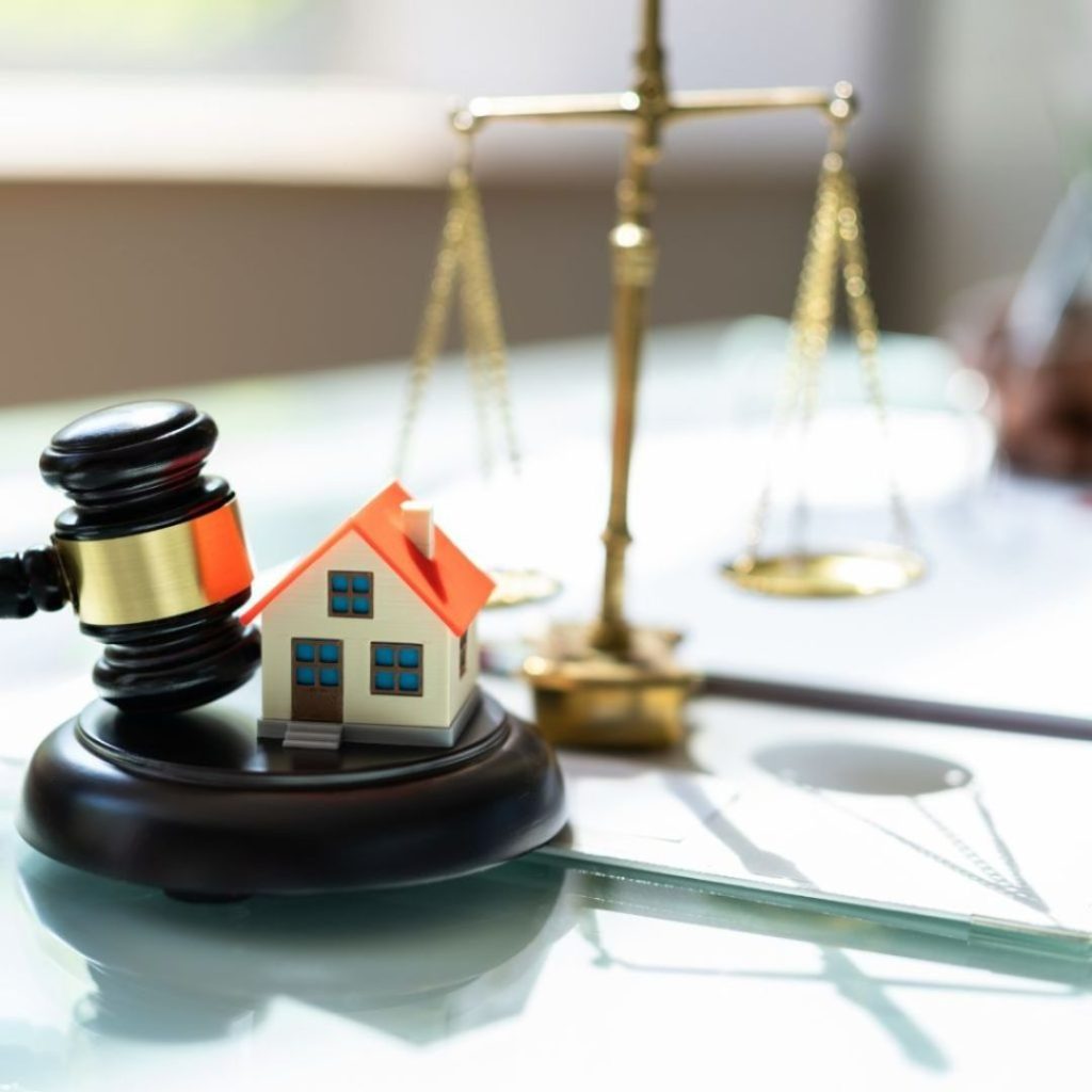 Gavel and house model with scales of justice in the background.