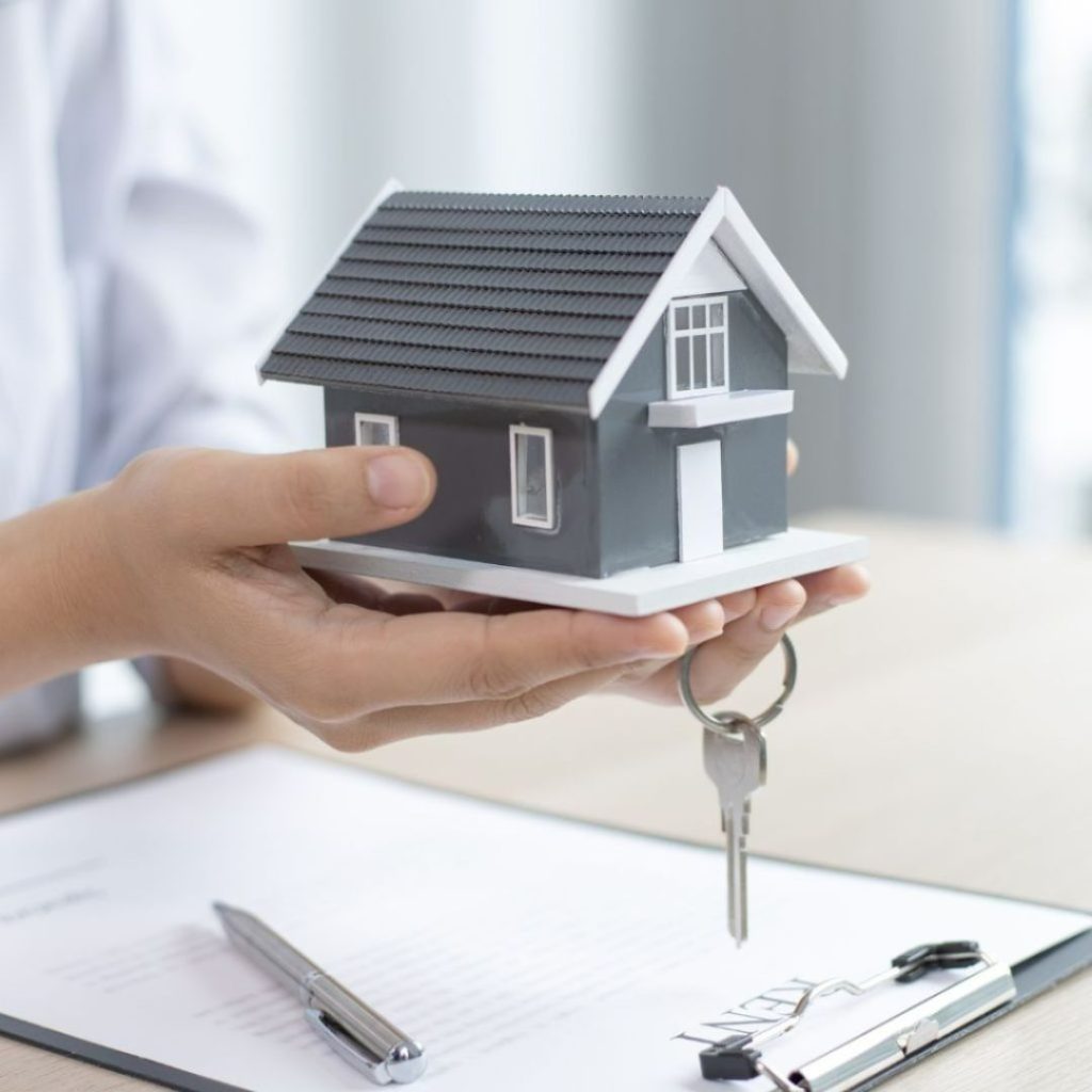 Hands holding a house model with keys above a contract