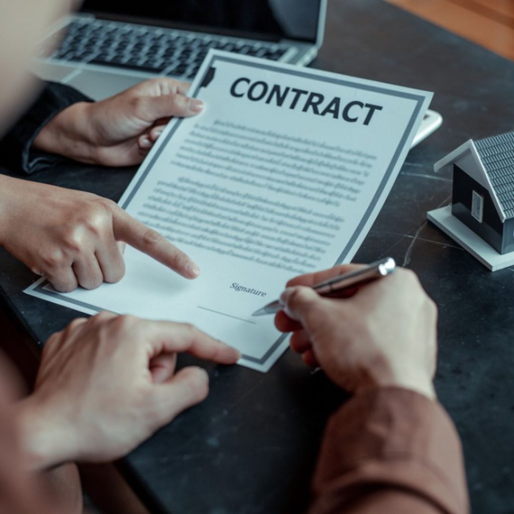 Person signing a real estate contract with a house model on the table