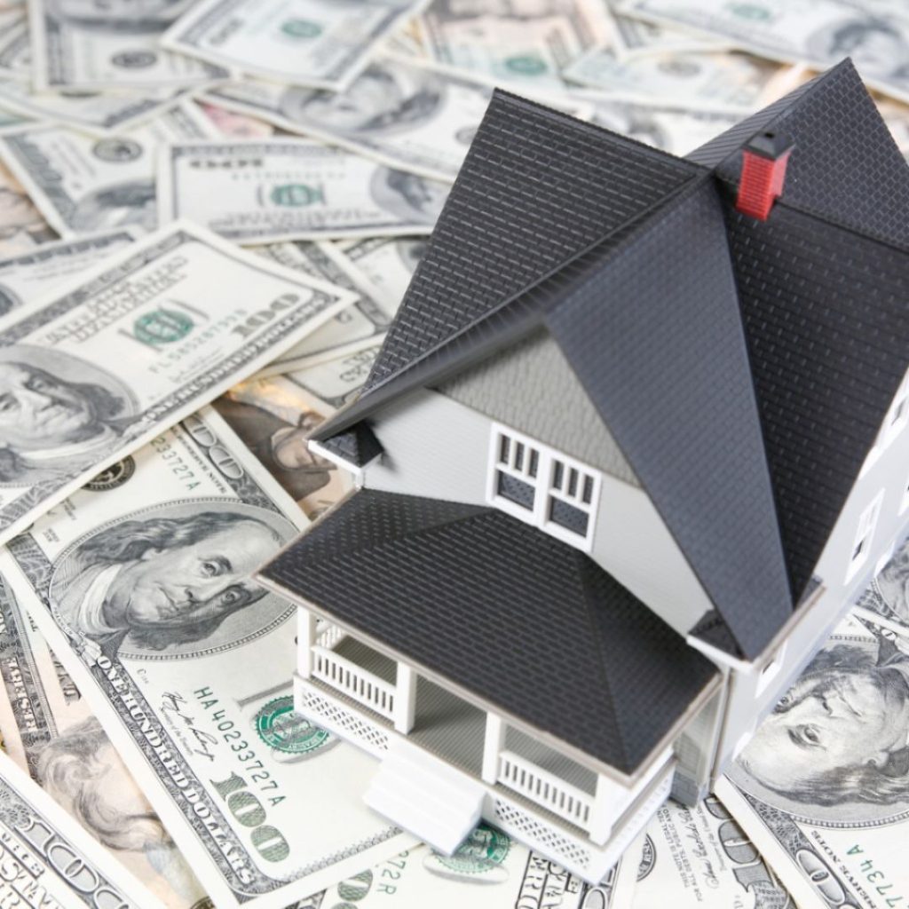 Miniature house model on top of scattered US dollar bills.