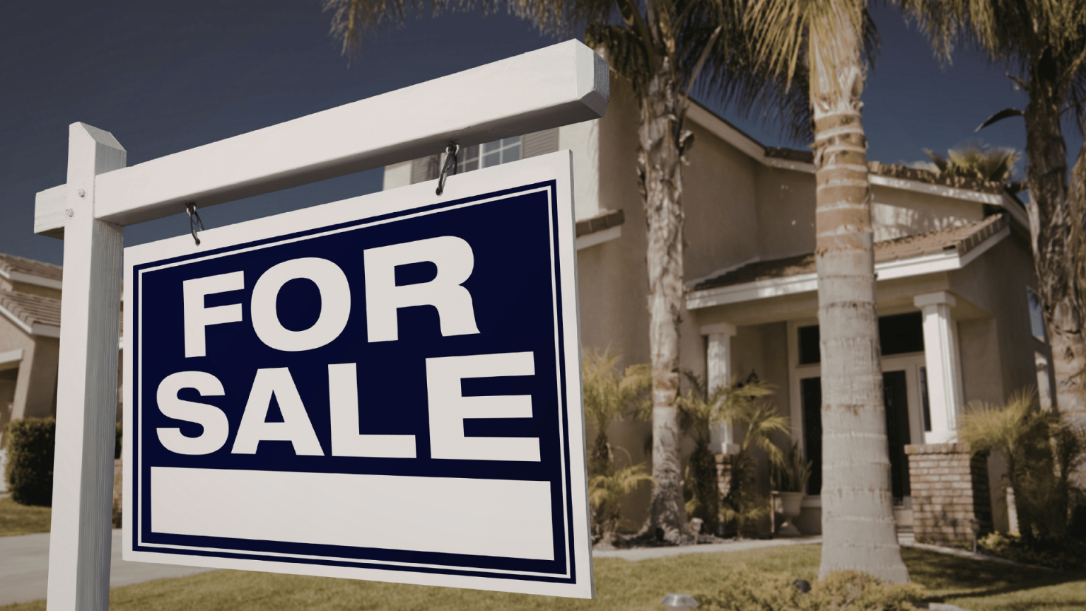 White and blue 'For Sale' yard sign placed in front of a suburban home with palm trees.