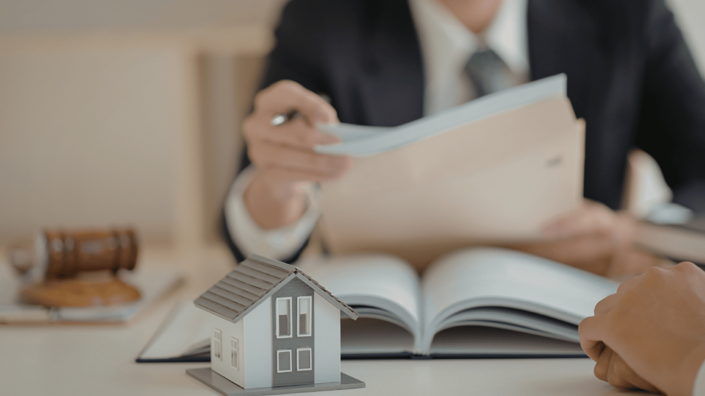 Real estate professional helping a home seller review closing documents alongside a miniature house model.