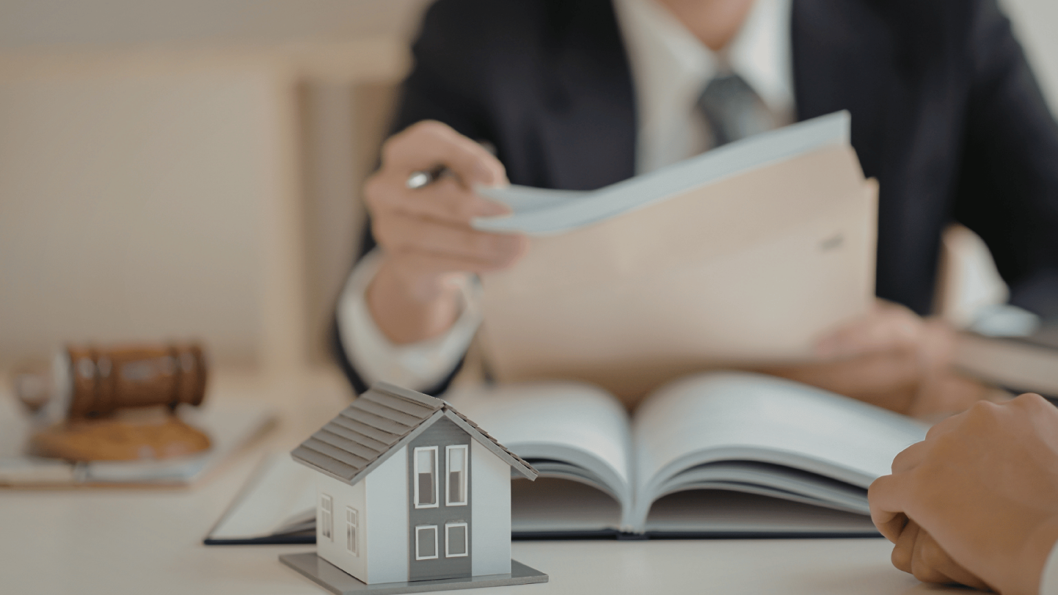 Real estate professional helping a home seller review closing documents alongside a miniature house model.