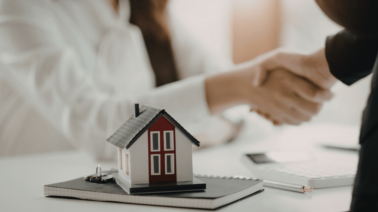Handshake finalizing a real estate transaction with a small house model and contract paperwork on a desk