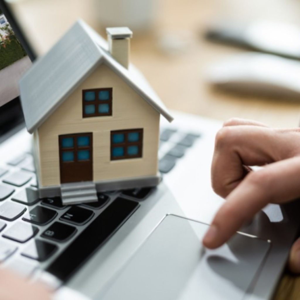 Mini house model on laptop keyboard for online real estate search.