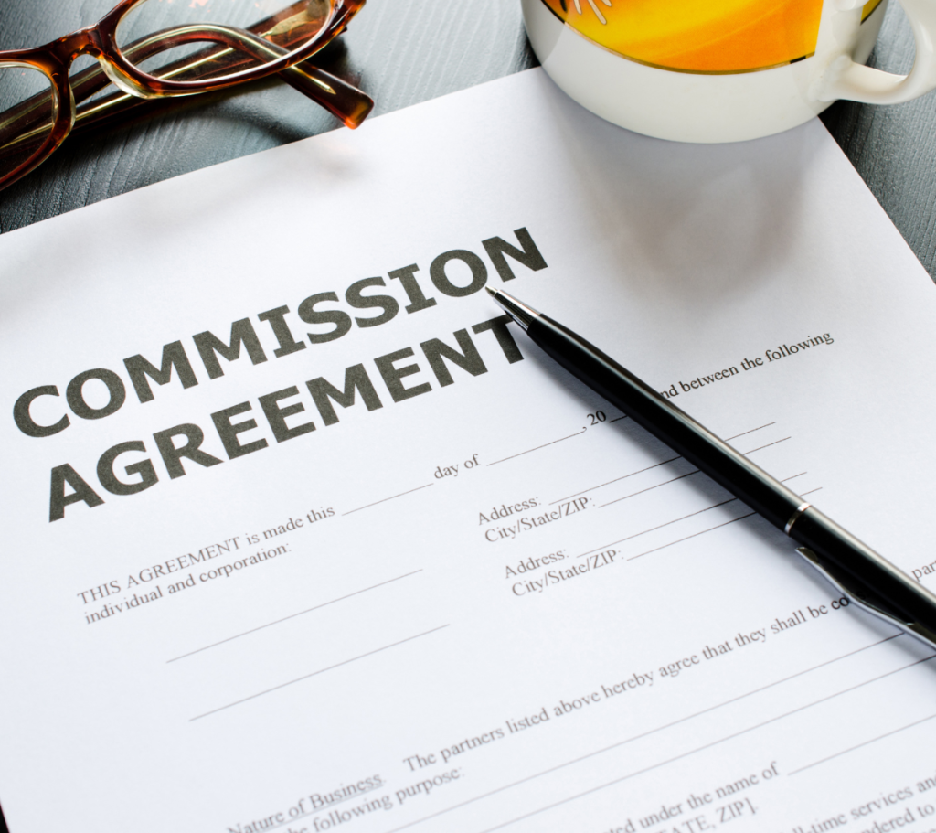 Commission agreement document with pen, glasses, and coffee cup.