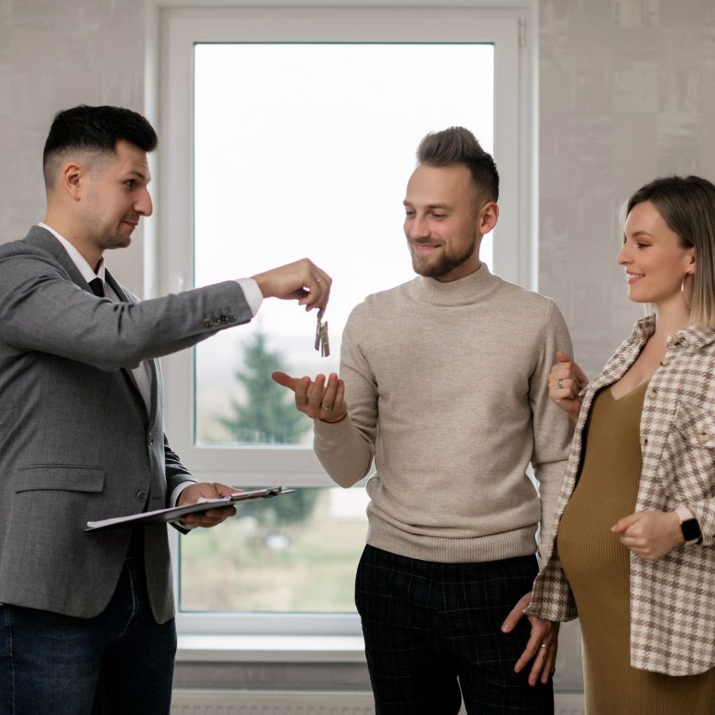 Real estate agent handing house keys to a smiling couple.