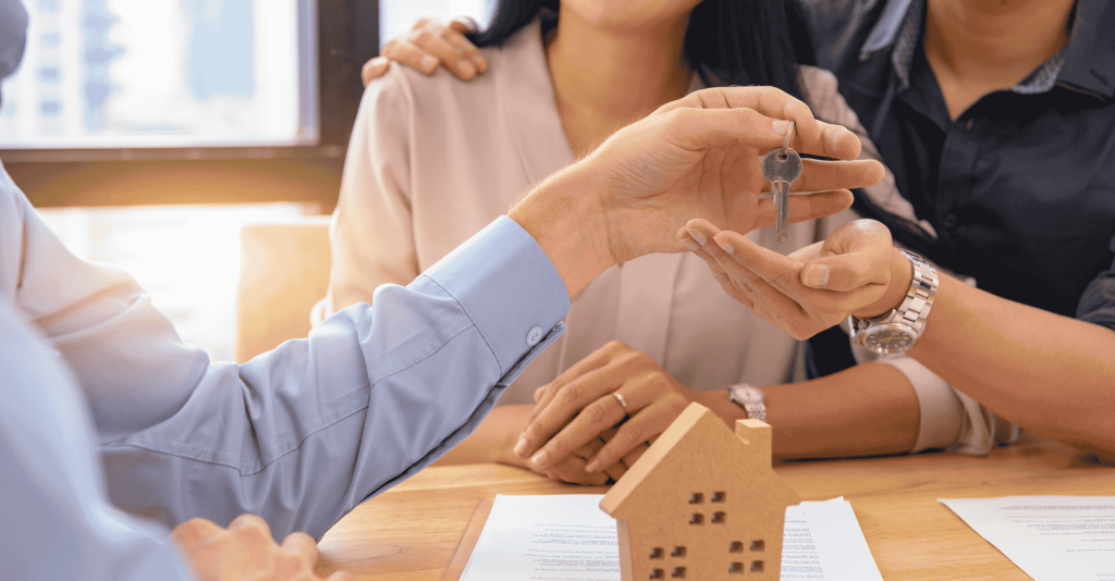 Real estate agent handing house keys to a smiling couple during a meeting, symbolizing a successful home purchase or closing.