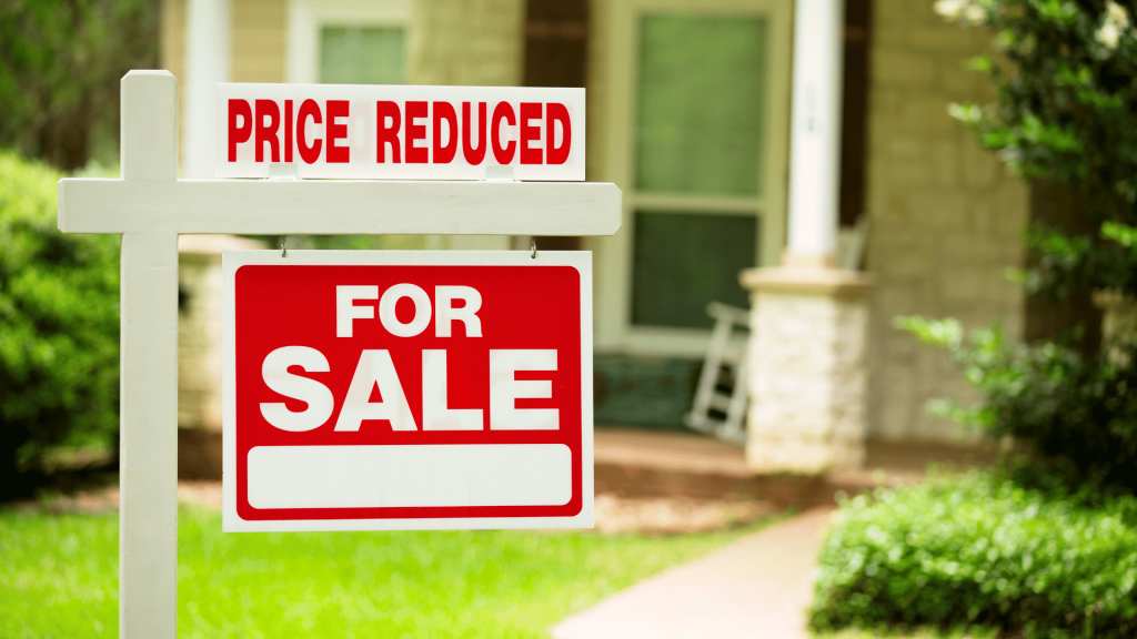 for sale sign with 'price reduced' sign above in front of house