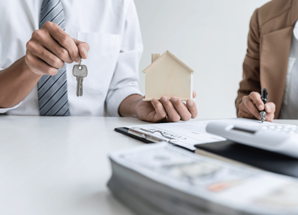 people at desk holding keys and house discussing paperwork