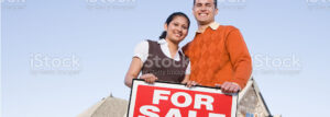 Man and woman standing in front of a house with a for sale sign.